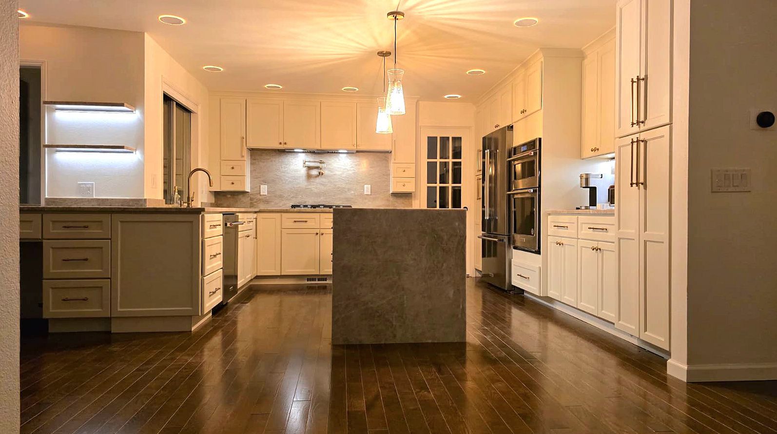 Finished kitchen remodel with white shaker cabinets, a stone waterfall island and pendant lights